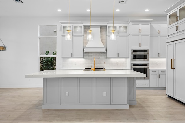 kitchen featuring a kitchen island with sink, pendant lighting, stainless steel appliances, and custom range hood