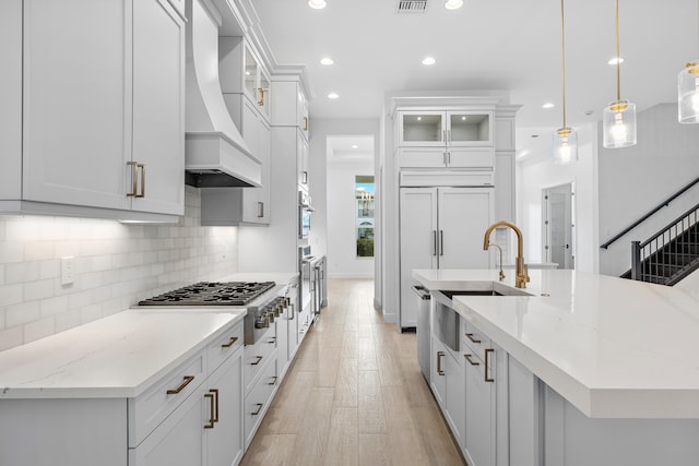 kitchen featuring light stone counters, premium range hood, light hardwood / wood-style floors, decorative light fixtures, and stainless steel gas stovetop