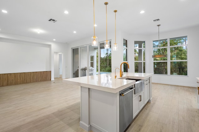 kitchen with pendant lighting, a kitchen island with sink, sink, light wood-type flooring, and white cabinetry