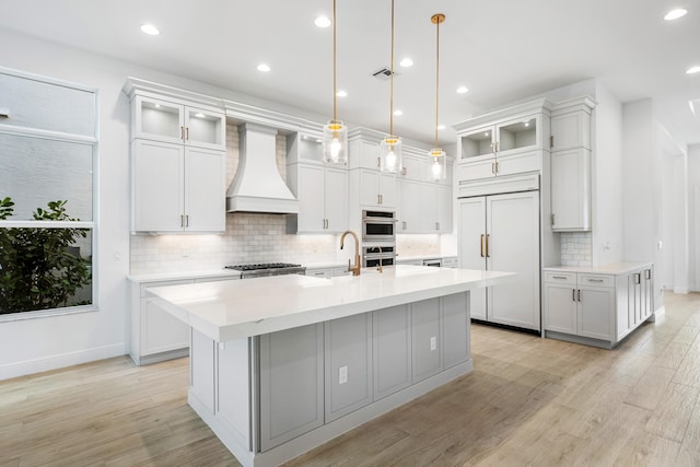 kitchen with premium range hood, a center island with sink, white cabinets, and light hardwood / wood-style floors