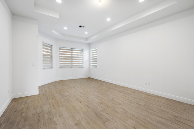 empty room featuring a raised ceiling and light hardwood / wood-style flooring