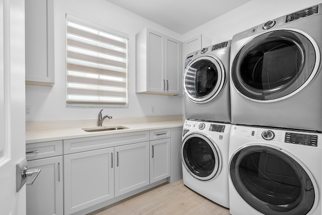 laundry area featuring cabinets, sink, washing machine and dryer, light hardwood / wood-style floors, and stacked washer / drying machine