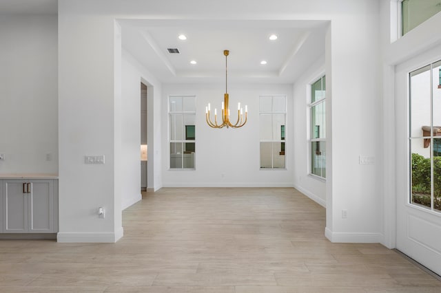 unfurnished dining area featuring a chandelier, light hardwood / wood-style flooring, and a tray ceiling