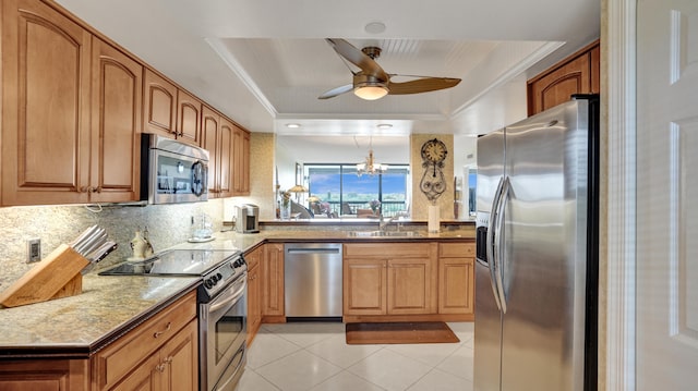 kitchen featuring light stone counters, pendant lighting, decorative backsplash, a tray ceiling, and appliances with stainless steel finishes