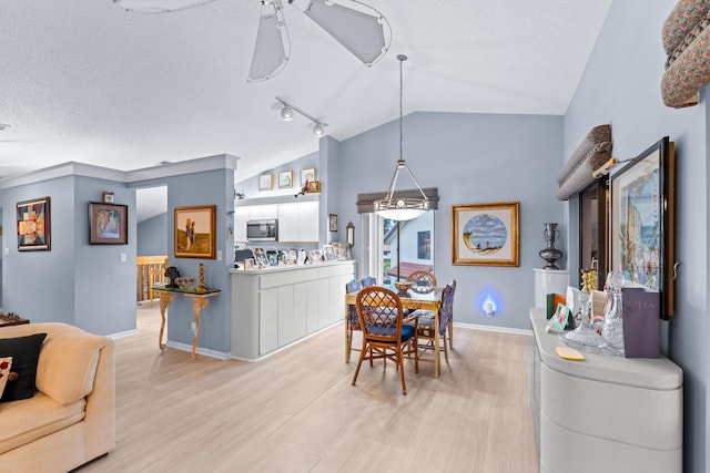 dining space with rail lighting, vaulted ceiling, ceiling fan, and a textured ceiling