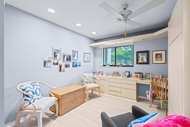 interior space with a textured ceiling, light hardwood / wood-style floors, built in desk, and ceiling fan