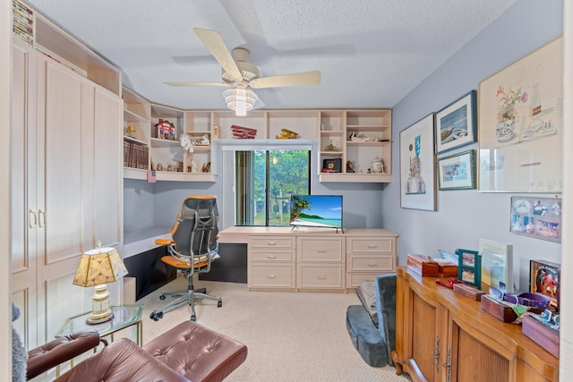 office area featuring a textured ceiling, light colored carpet, built in desk, and ceiling fan