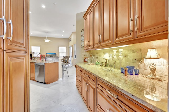 kitchen with tasteful backsplash, light stone counters, light tile patterned floors, sink, and dishwasher