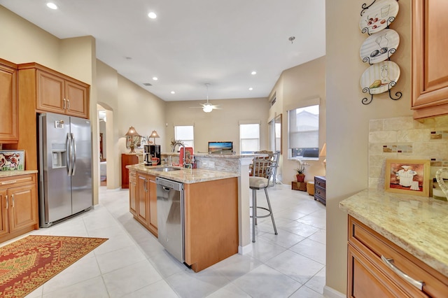 kitchen featuring a kitchen bar, stainless steel appliances, light tile patterned floors, and light stone countertops