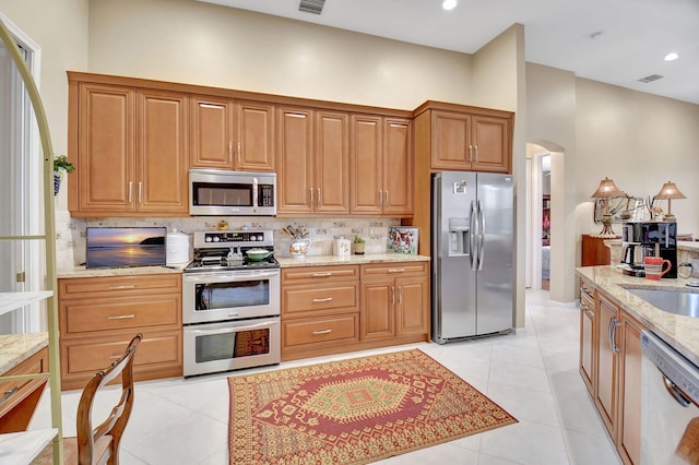 kitchen with sink, appliances with stainless steel finishes, light stone countertops, light tile patterned floors, and decorative backsplash