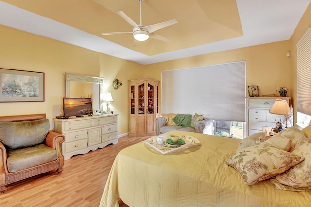 bedroom featuring ceiling fan, a raised ceiling, and light hardwood / wood-style flooring