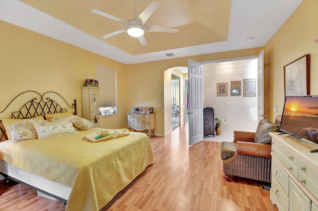 bedroom with light wood-type flooring, ceiling fan, and a raised ceiling