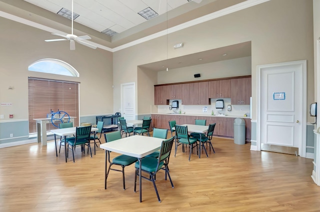 dining space with a towering ceiling, light hardwood / wood-style flooring, ceiling fan, and crown molding