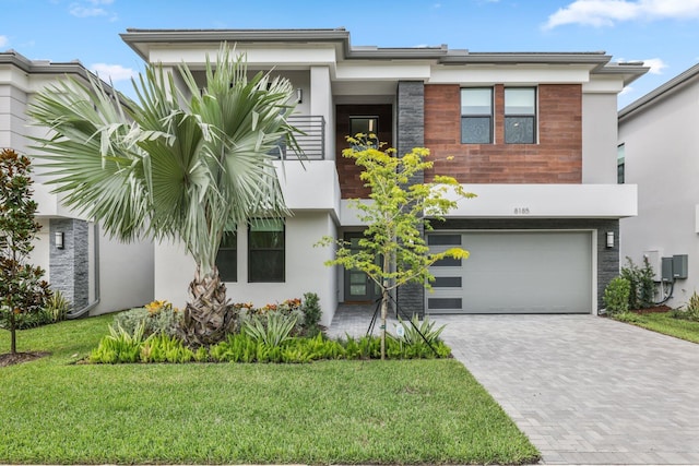 view of front facade with a front yard, decorative driveway, an attached garage, and stucco siding