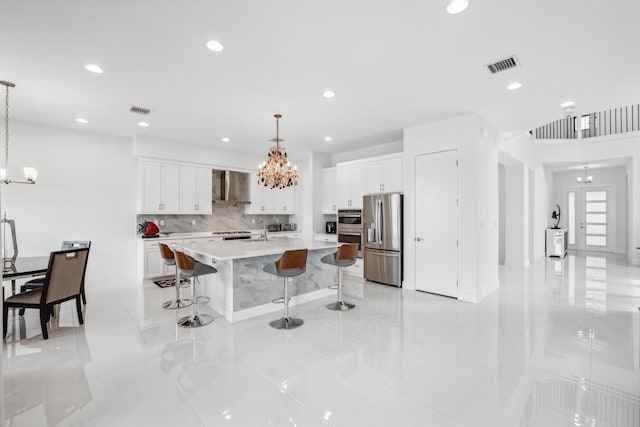 kitchen featuring visible vents, appliances with stainless steel finishes, a breakfast bar area, wall chimney range hood, and a chandelier