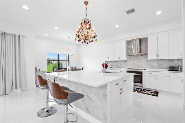 kitchen featuring visible vents, an inviting chandelier, stainless steel oven, wall chimney range hood, and a sink