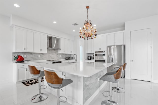 kitchen with a sink, white cabinets, wall chimney range hood, appliances with stainless steel finishes, and tasteful backsplash