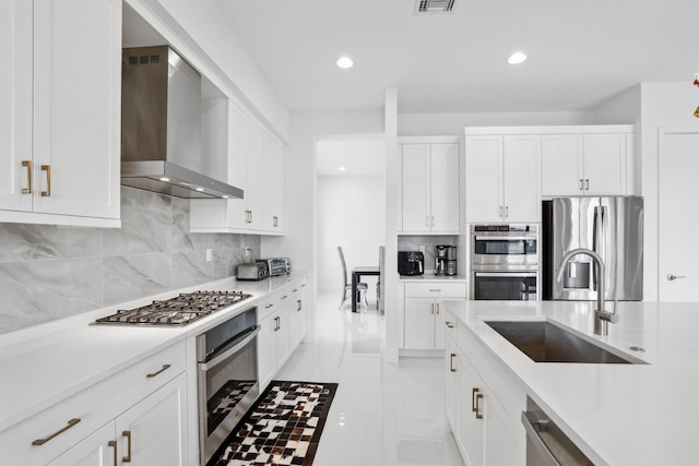 kitchen with tasteful backsplash, appliances with stainless steel finishes, light countertops, wall chimney range hood, and a sink