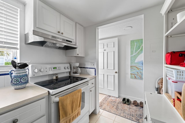 kitchen featuring white range with electric stovetop, light tile patterned flooring, white cabinetry, and a textured ceiling