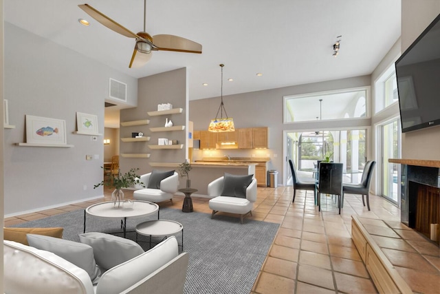 tiled living room featuring ceiling fan, a high ceiling, and a tiled fireplace