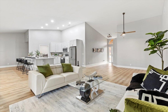 living room with ceiling fan, high vaulted ceiling, and light hardwood / wood-style flooring