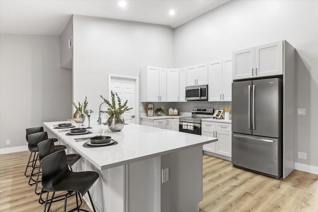 kitchen featuring appliances with stainless steel finishes, a kitchen breakfast bar, light hardwood / wood-style flooring, a high ceiling, and white cabinetry