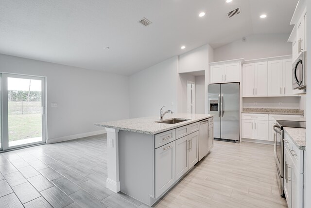 kitchen with sink, appliances with stainless steel finishes, a kitchen island with sink, white cabinets, and vaulted ceiling