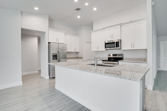 kitchen with stainless steel appliances, a center island with sink, sink, white cabinets, and vaulted ceiling