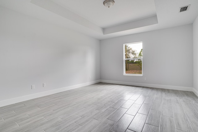 empty room with a raised ceiling and light hardwood / wood-style flooring