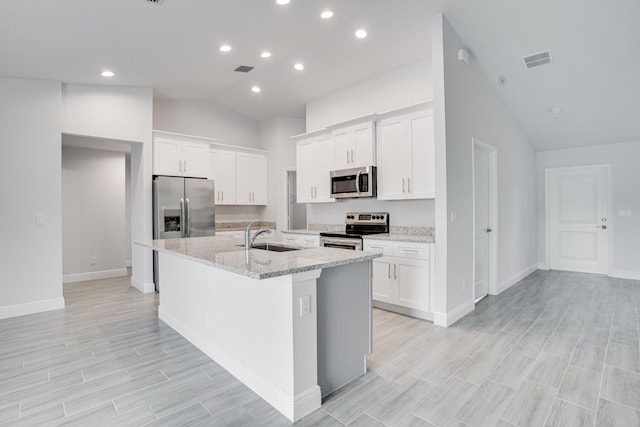 kitchen featuring a center island with sink, stainless steel appliances, light wood-type flooring, light stone countertops, and white cabinets