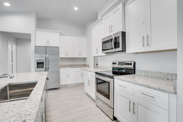 kitchen with white cabinetry, sink, light stone counters, appliances with stainless steel finishes, and lofted ceiling