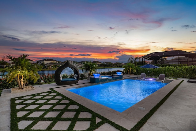 pool at dusk featuring pool water feature, a patio area, and an in ground hot tub