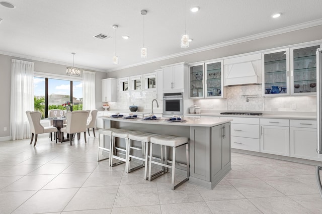 kitchen with custom exhaust hood, oven, a center island with sink, white cabinetry, and hanging light fixtures