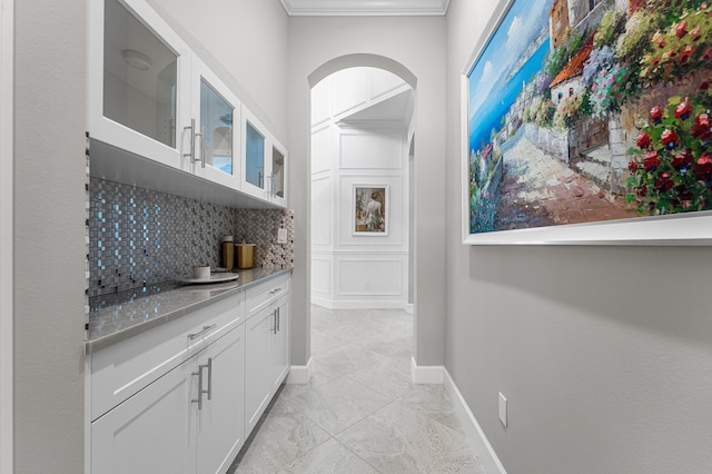 bar with white cabinets, decorative backsplash, light stone counters, and crown molding