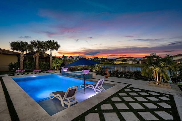 pool at dusk with a patio area and an in ground hot tub