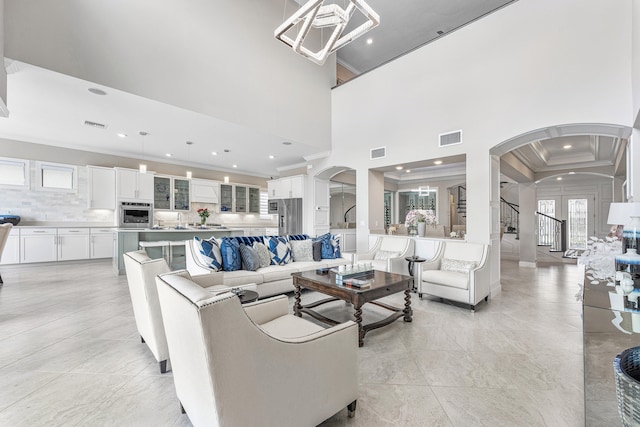 living room with crown molding, sink, a towering ceiling, and a notable chandelier