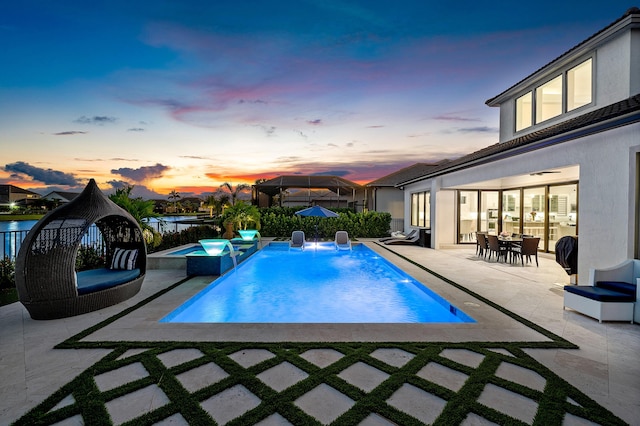 pool at dusk with a jacuzzi, pool water feature, and a patio area