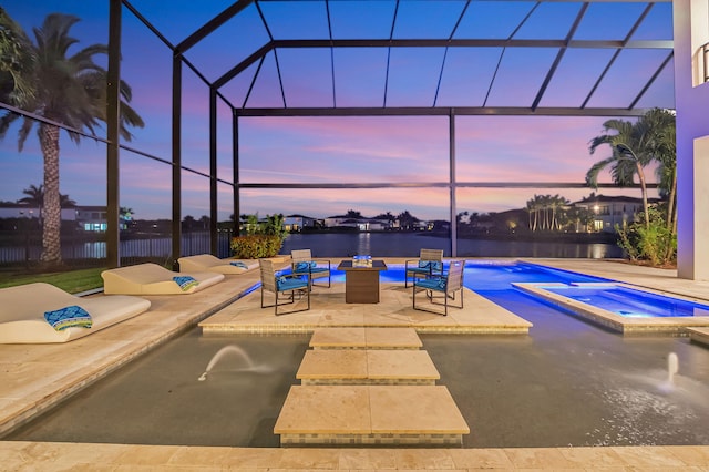 pool at dusk featuring a water view, an in ground hot tub, glass enclosure, and a patio area