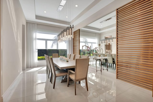 tiled dining area featuring a raised ceiling and a chandelier