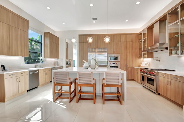 kitchen featuring wall chimney exhaust hood, a breakfast bar, high end appliances, and a center island with sink