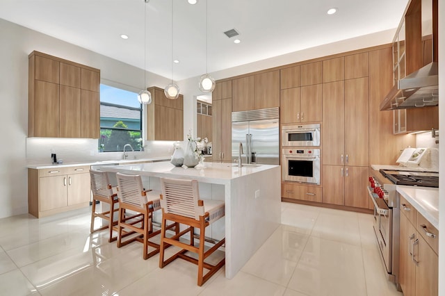 kitchen with a kitchen island with sink, a breakfast bar area, light tile patterned floors, high quality appliances, and pendant lighting