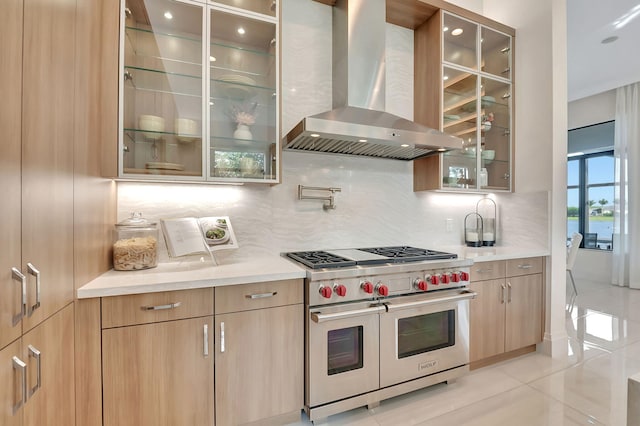 kitchen with light tile patterned floors, range with two ovens, decorative backsplash, light brown cabinets, and range hood