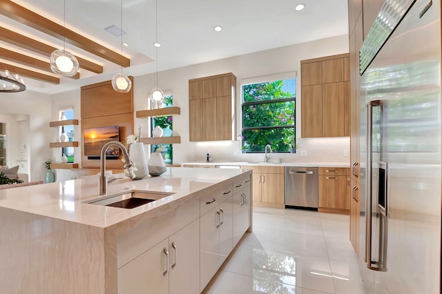 kitchen featuring decorative light fixtures, stainless steel appliances, a kitchen island with sink, white cabinets, and sink