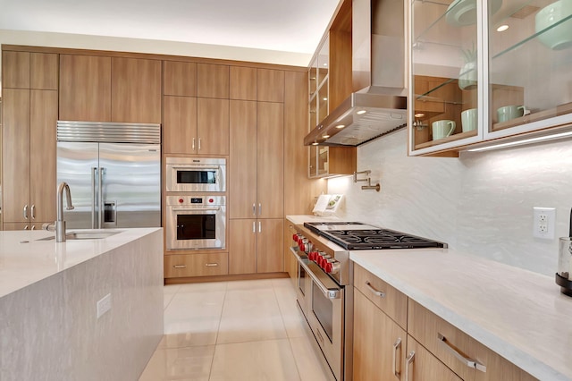 kitchen with premium appliances, island exhaust hood, tasteful backsplash, light tile patterned flooring, and sink