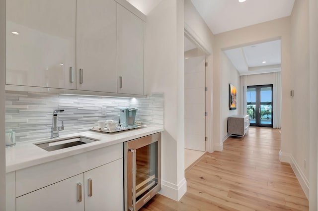 bar featuring sink, decorative backsplash, beverage cooler, and light hardwood / wood-style flooring