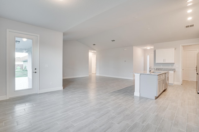 interior space featuring light stone countertops, an island with sink, white cabinets, light wood-type flooring, and vaulted ceiling