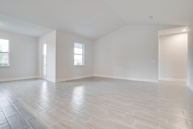 empty room featuring light hardwood / wood-style flooring, vaulted ceiling, and plenty of natural light