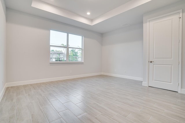 spare room featuring light wood-type flooring and a raised ceiling