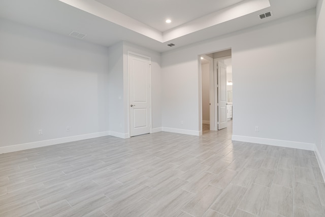 spare room with light hardwood / wood-style floors and a raised ceiling