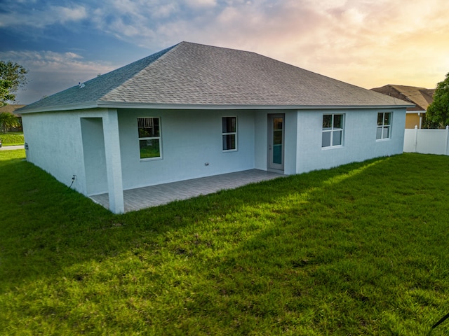 back house at dusk with a patio area and a lawn